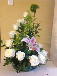 a vase filled with white flowers and greenery on top of a table next to a wall