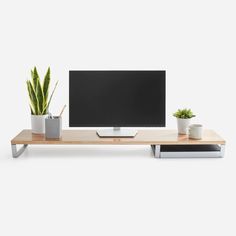 a flat screen tv sitting on top of a wooden shelf next to potted plants