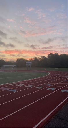 the sun is setting on an empty track in a field with red and white markings