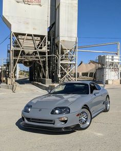 a silver sports car is parked in front of a large silo and some buildings