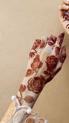 a woman's hand with henna and flowers painted on her arm, holding something in the other hand