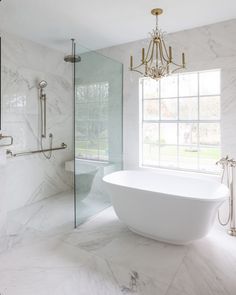 a white bath tub sitting next to a window in a bathroom under a chandelier