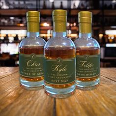 three bottles of whisky sitting on top of a wooden table in front of a bar