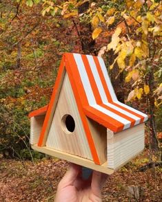 a birdhouse with an orange and white striped roof is held up by a hand