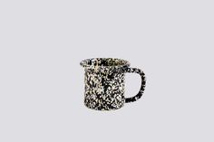 a black and white coffee mug with speckles on the inside, in front of a gray background