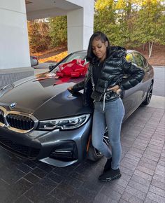 a woman standing next to a bmw car with her hand up in the air and smiling