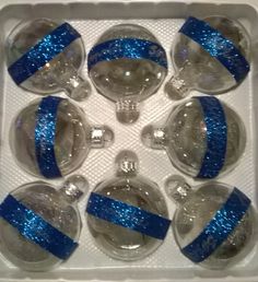 six glass ornaments in a box with blue ribbon around the ornament and silver balls