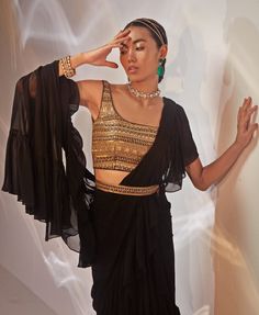 Introducing the stunning Black Ruffled Georgette Saree set seamlessly blends traditional charm with modern sophistication. Crafted from luxurious georgette fabric, the black saree drapes effortlessly, creating a flattering, fluid silhouette. Paired with a meticulously hand-embellished blouse, this ensemble exudes glamour through its intricate detailing. A matching embellished belt cinches the waist, adding a contemporary twist to the classic saree. This style is a ready to wear saree for your ease. Perfect for Cocktails, this outfit truly shines when complemented with statement jewellery and stylish heels. Composition : Saree, Blouse - Georgette Care: Dry Clean Only and Vacuum Storage This product can be customized for sleeves, blouse length and neckline Delivery : 4-6 weeks as the product Black Georgette Draped Saree, Black Draped Georgette Saree, Party Wear Draped Sharara With Cutdana, Party Sharara With Cutdana And Draped Design, Festive Draped Georgette Blouse, Black Draped Saree With Sheer Dupatta, Black Blouse With Dupatta For Reception, Georgette Blouse With Traditional Drape For Evening, Evening Blouse In Georgette With Traditional Drape