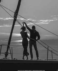 two people standing on the top of a boat at sunset with their arms in the air