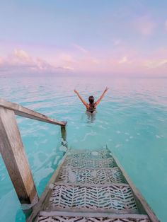 a woman standing in the ocean with her arms spread out and hands raised above her head