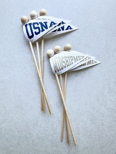 three wooden sticks with white and blue stickers on them, one has the word usna written on it