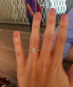 a woman's hand with a diamond ring on her left hand and a man in the background