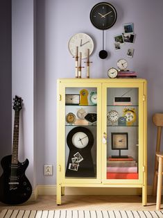 a yellow cabinet with several clocks on the wall and a guitar in front of it