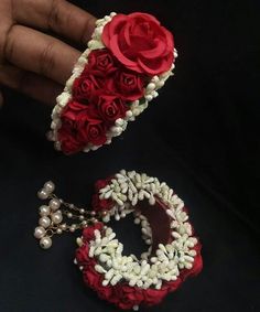 two bracelets with red roses and pearls on them, one is being held by someone's hand