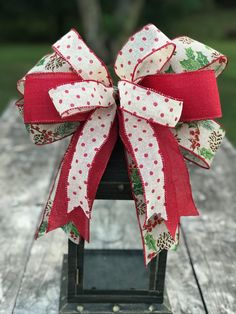 a red and white christmas bow on top of a wooden table with trees in the background