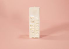 a white candle with the word mom written on it in front of a pink background