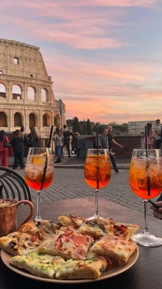 three glasses of wine and pizza on a table in front of the colossion