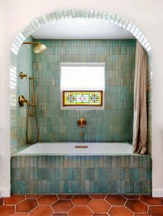 a bath tub sitting under a window next to a tiled wall and floor in a bathroom