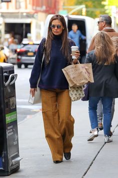 a woman is walking down the street carrying shopping bags and holding a coffee in her hand