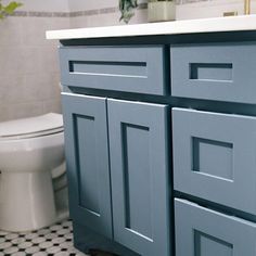 a white toilet sitting next to a blue cabinet in a bathroom with black and white checkered flooring