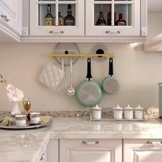 a kitchen with white cabinets and marble counter tops, pots and pans hanging on the wall