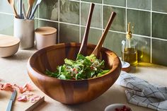 a wooden bowl filled with green salad on top of a counter next to utensils