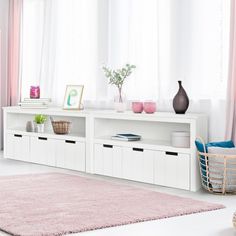 a living room with white furniture and pink curtains on the window sill, along with a rug