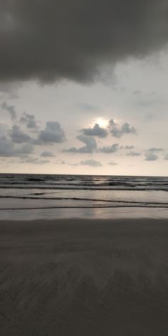 the sun is setting over the ocean with dark clouds in the sky, and some people are walking on the beach