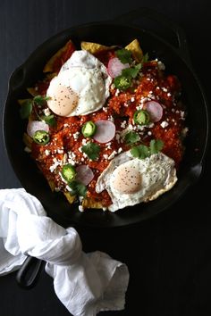 two fried eggs are in a skillet with tomato sauce and other toppings on the side