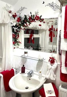 a bathroom decorated in red and white with christmas decorations on the window sill, toiletries, sink, towel rack and mirror