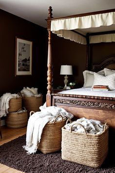 a canopy bed in a bedroom with baskets on the floor next to it and two lamps