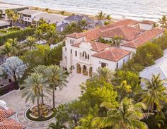 an aerial view of a mansion with palm trees and ocean in the background