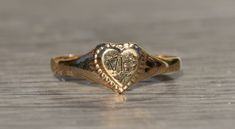 The Evart Children's Yellow Gold Heart Ring. Crafted in yellow gold, this child's ring features an engraved heart with the initials EG. We can remove the initials and add engraving of your choice for an additional charge. The ring is currently a finger size 3.5 and is able to be resized for an additional charge, as well. Each piece has been hand selected and meticulously identified and graded by a Graduate Gemologist who has been awarded a degree by the Gemological Institute of America (GIA). Pl Yellow Gold Engraved Ring With Initials For Promise, Personalized Engraved Heart Ring For Promise, Antique Personalized Engraved Wedding Ring, Yellow Gold Engraved Initial Ring For Promise, Valentine's Day Engraved Signet Promise Ring, Heirloom Heart Shaped Engraved Promise Ring, Heirloom Heart-shaped Engraved Promise Ring, Personalized Antique Engraved Wedding Ring, Vintage Engraved Ring With Initials For Promise