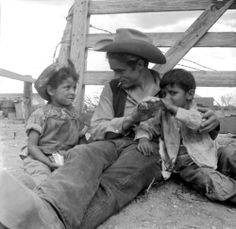 a woman sitting on the ground next to two children with a pipe in their mouth