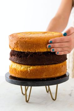 a woman holding a cake on top of a black plate with two layers and chocolate frosting