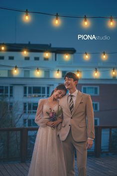 a man and woman standing next to each other on a wooden deck with lights strung above them