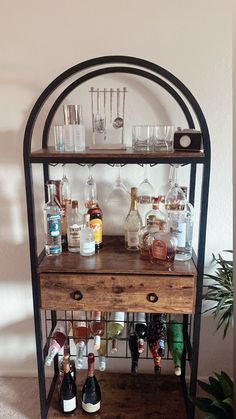 an old bar cart with liquor bottles and glasses on it's shelf, next to a potted plant