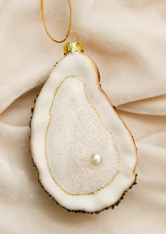 an ornament is hanging on a white sheet with gold trimmings and a pearl in the center