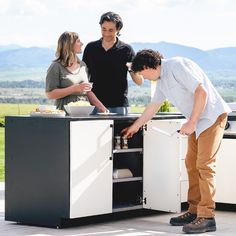 three people standing around an outdoor kitchen preparing food