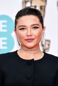 a woman with short hair wearing a black dress and large earrings on her head, posing for the camera