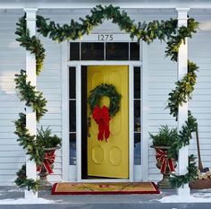 a yellow front door decorated with christmas wreaths