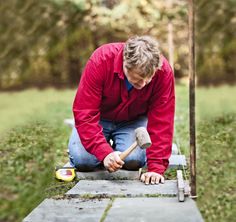 a man kneeling down with a hammer in his hand next to a piece of wood