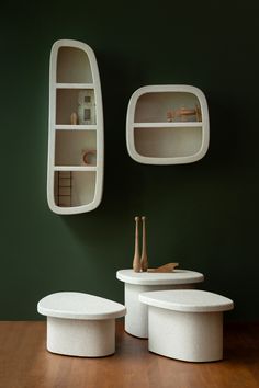 two white round tables with shelves on the wall behind them, and an oval shaped shelf above it