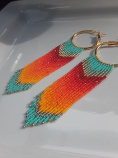 two pairs of colorful beaded earrings sitting on top of a white plate with gold hoop