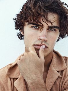 a young man with curly hair and blue eyes is holding his finger to his mouth