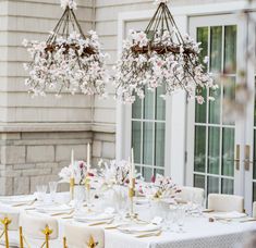 the table is set with white linens and gold place settings, along with floral centerpieces