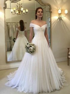 a woman standing in front of a mirror wearing a wedding dress with off the shoulder sleeves