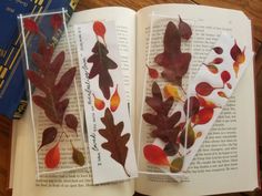 two bookmarks with leaves on them sitting on top of an open book next to a pile of books