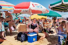 people sitting under umbrellas at the beach on a sunny day with coolers and chairs