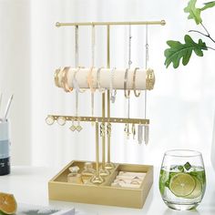 a gold jewelry holder with rings, bracelets, and other items on it next to a glass of water